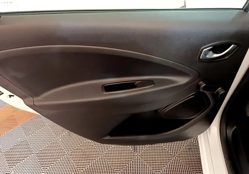 Vue rapprochée de la porte intérieure côté droit noire de la Renault ZOE blanche, avec poignée et haut-parleur intégrés.