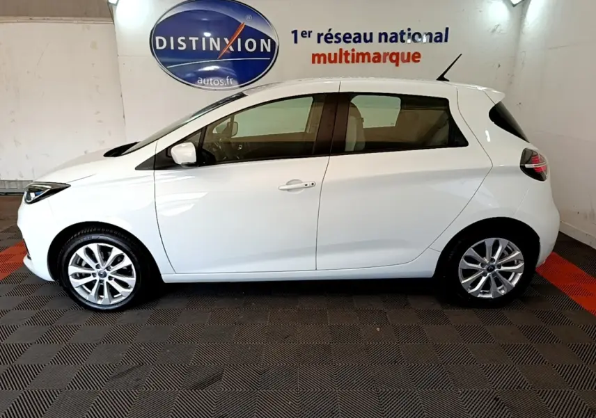 Profil côté gauche de la Renault ZOE Zen R110 blanche, compacte et électrique, sur fond intérieur avec logo Distinxion.