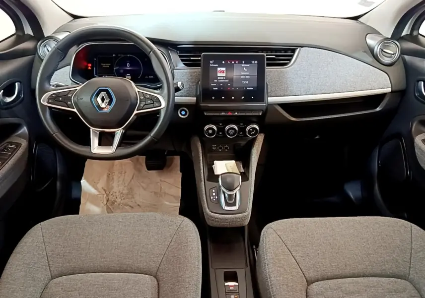 Vue intérieure avant de la Renault ZOE Zen R110 blanche, tableau de bord avec écran tactile central et volant multifonctions.