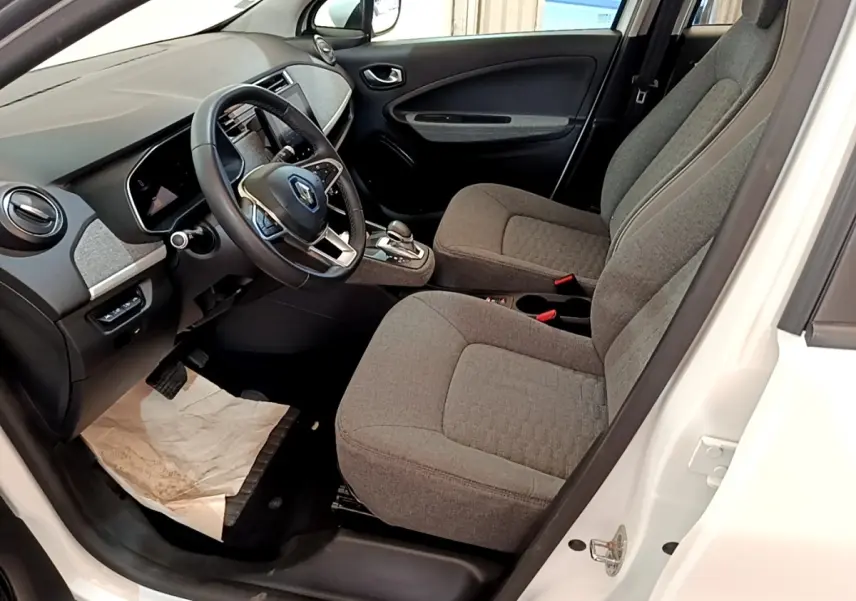 Vue intérieure côté conducteur de la Renault ZOE blanche 2019, sièges gris et tableau de bord avec écran tactile.