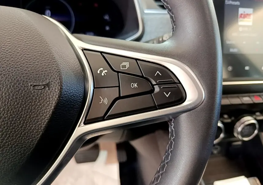 Gros plan sur les commandes multifonctions du volant en cuir noir de la Renault ZOE blanche, avec écran tactile en arrière-plan.