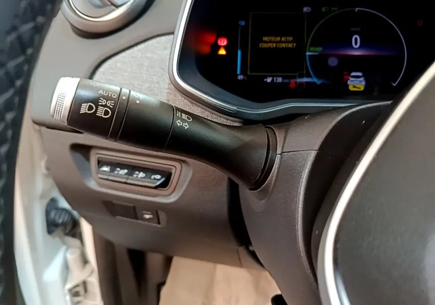 Gros plan sur la commande des phares et clignotants à gauche du volant dans le tableau de bord numérique d’une Renault ZOE blanche.