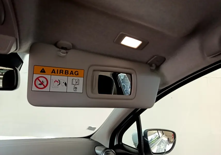 Vue intérieure du pare-soleil côté conducteur avec miroir et étiquette airbag, rétro extérieur visible, habitacle clair.