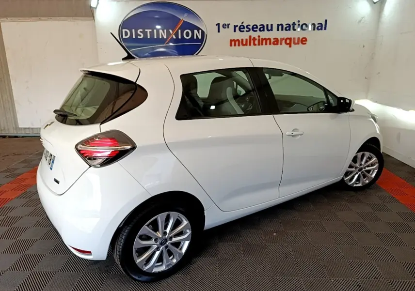 Vue 3/4 arrière droite d'une Renault ZOE Zen R110 blanche électrique, avec feux arrière LED et jantes alliage visibles.