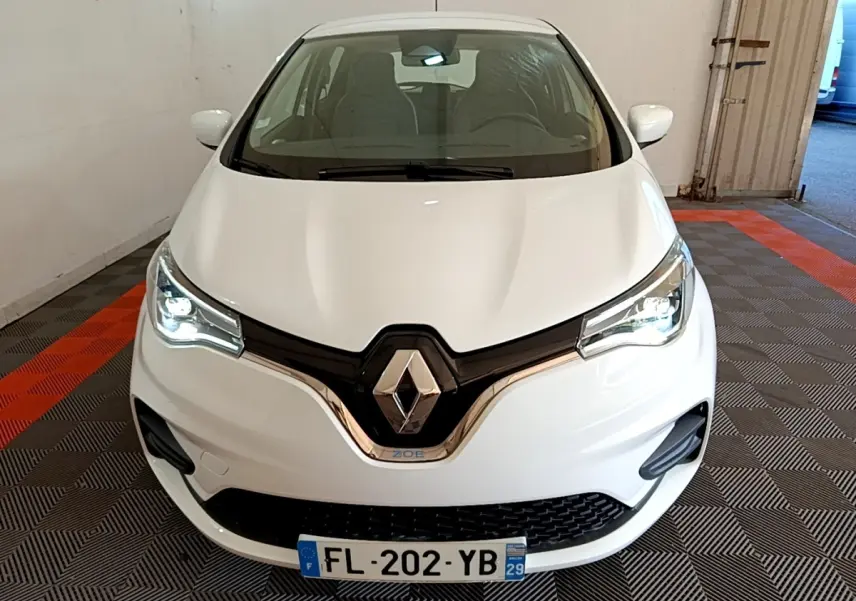 Vue avant d'une Renault ZOE blanche 2019 avec phares LED allumés et logo Renault bien visible.