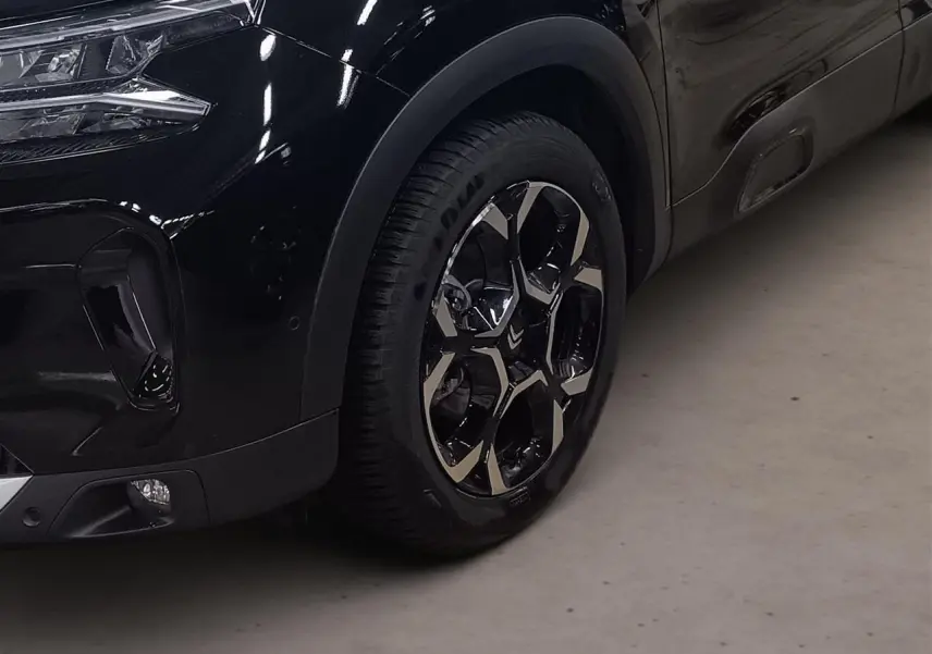 Gros plan sur la roue avant gauche et le pare-chocs noir Perla du Citroën C5 Aircross Hybrid 2025.