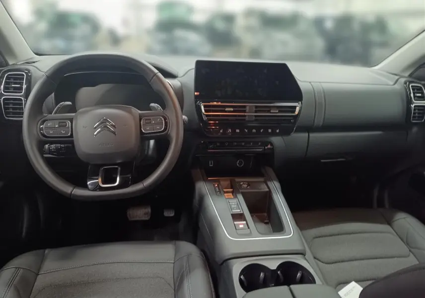 Vue intérieure avant du Citroën C5 Aircross Hybrid noir Perla, avec volant cuir et écran tactile central noir brillant.