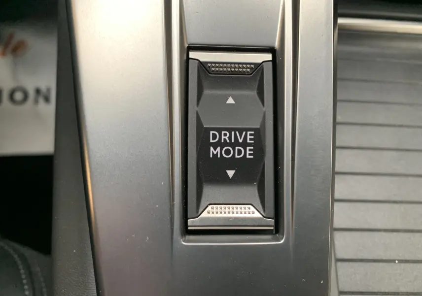 Gros plan sur le bouton Drive Mode au centre de la console d'une Peugeot 308 GT PHEV blanc nacré.