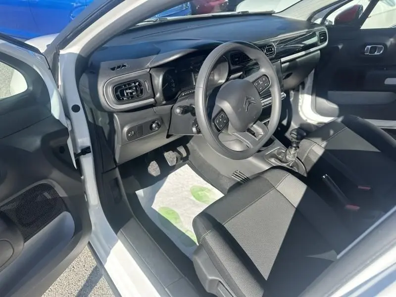 Intérieur côté conducteur d'une Citroën C3 blanche 2021 avec tableau de bord noir et boîte manuelle visible