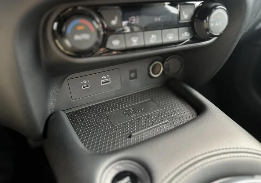 Gros plan sur la console centrale du Nissan Juke 2025, montrant les ports USB, prise 12V et zone de charge sans fil.
