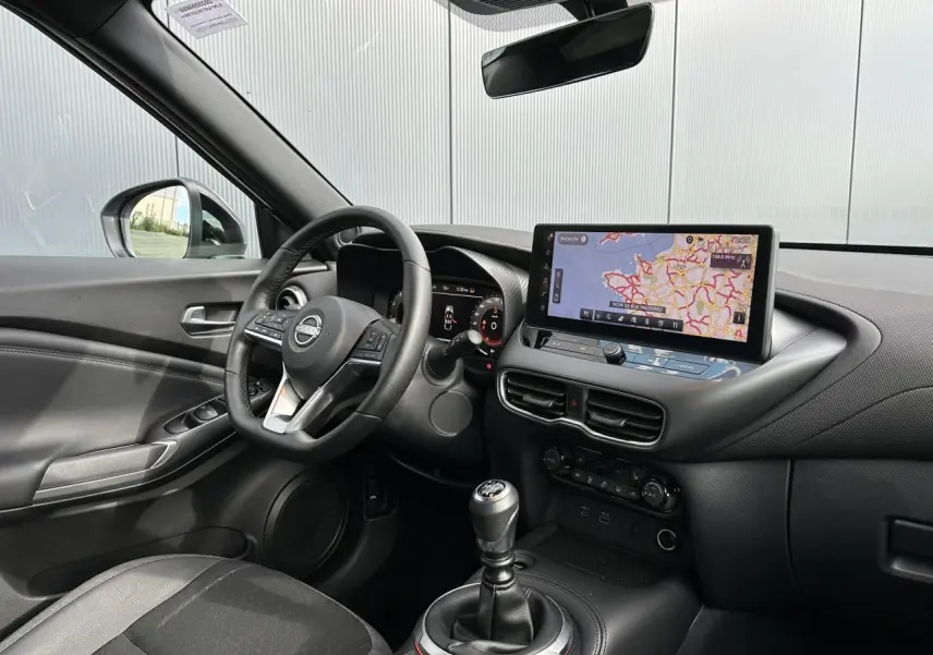 Intérieur noir du Nissan Juke 2025 vu côté conducteur, avec tableau de bord digital et écran tactile GPS.