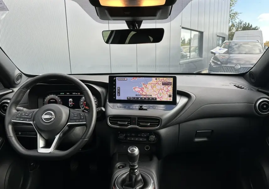 Vue intérieure frontale du tableau de bord noir du Nissan Juke blanc nacré avec écran tactile et levier de vitesse manuel.