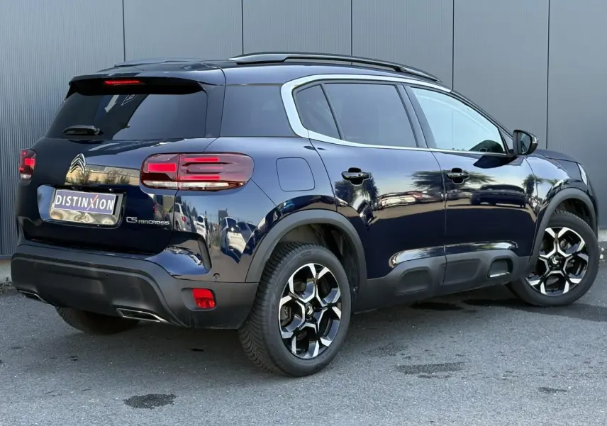 Vue 3/4 arrière droite du Citroën C5 Aircross bleu Eclipse avec jantes alliage bi-ton et barres de toit noires.
