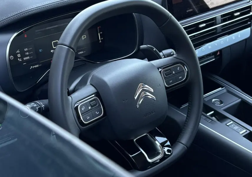 Vue rapprochée du volant en cuir noir et du tableau de bord numérique du Citroën C5 Aircross Hybrid 2025.