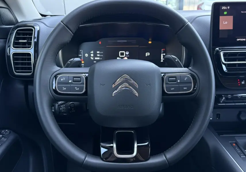 Vue rapprochée du volant noir de la Citroën C5 Aircross Hybrid 2025 avec commandes intégrées et tableau de bord numérique.