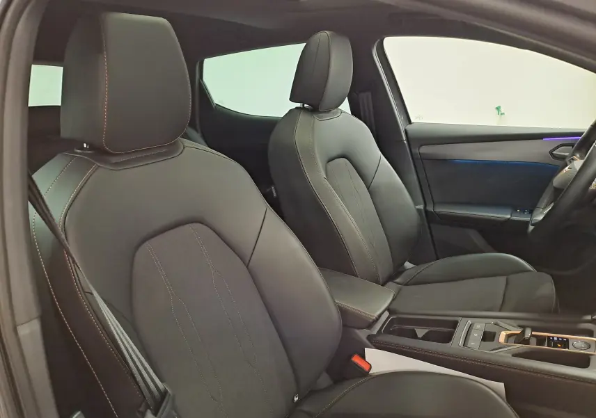 Vue intérieure côté conducteur et passager avant de la CUPRA Leon 1.5 eTSI 150 DSG7 avec sièges noirs et surpiqûres cuivrées.