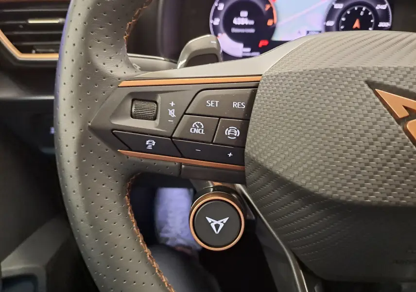 Gros plan sur le volant perforé de la CUPRA Leon 2025 avec commandes intégrées et surpiqûres cuivrées distinctives.