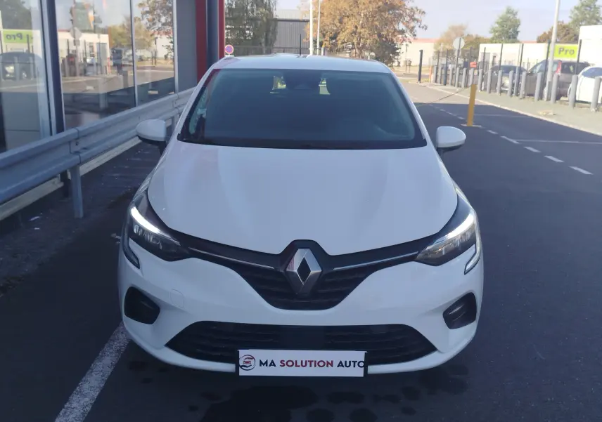 Vue avant d'une Renault Clio Business blanche de 2021 avec feux LED allumés, stationnée devant un bâtiment.