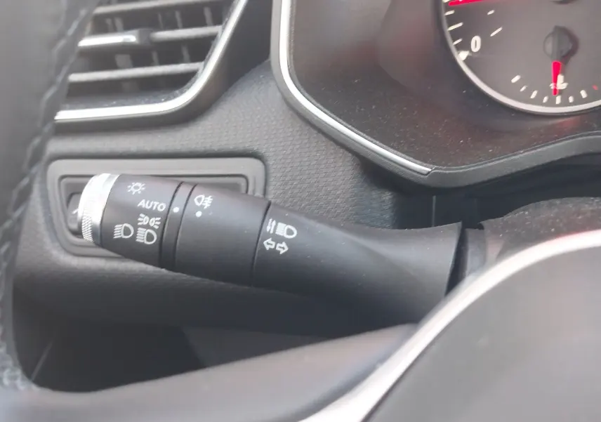 Gros plan sur la commande des phares et clignotants à gauche du volant dans l’habitacle gris d’une Renault Clio blanche 2021.