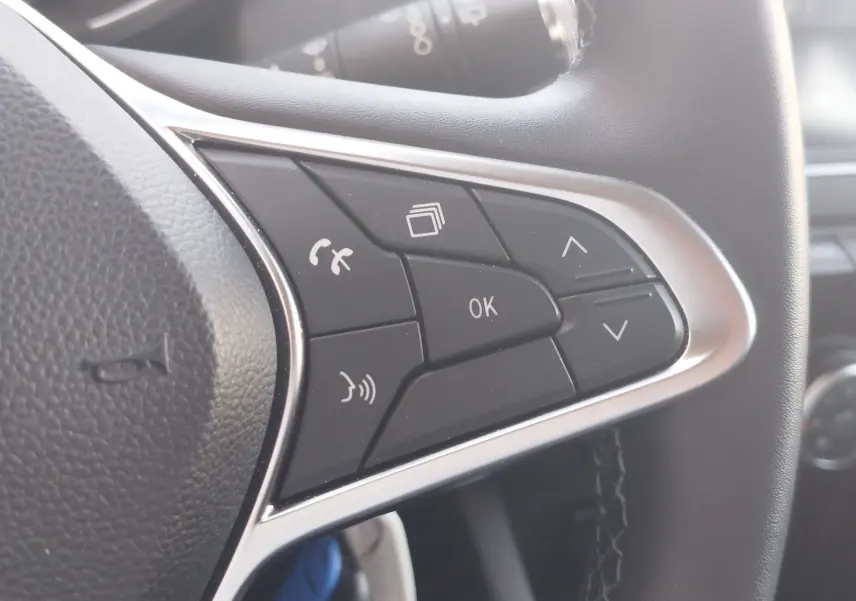 Gros plan sur les commandes multifonctions côté gauche du volant noir de la Renault Clio Business blanche de 2021.
