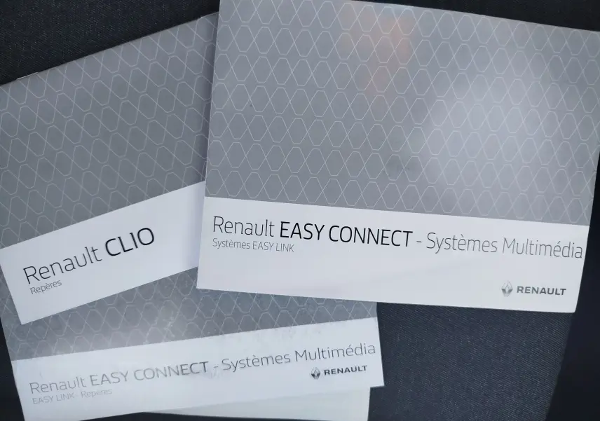 Image non conforme à la description d'un véhicule, montrant des brochures Renault Clio et Easy Connect posées sur un tissu sombre.