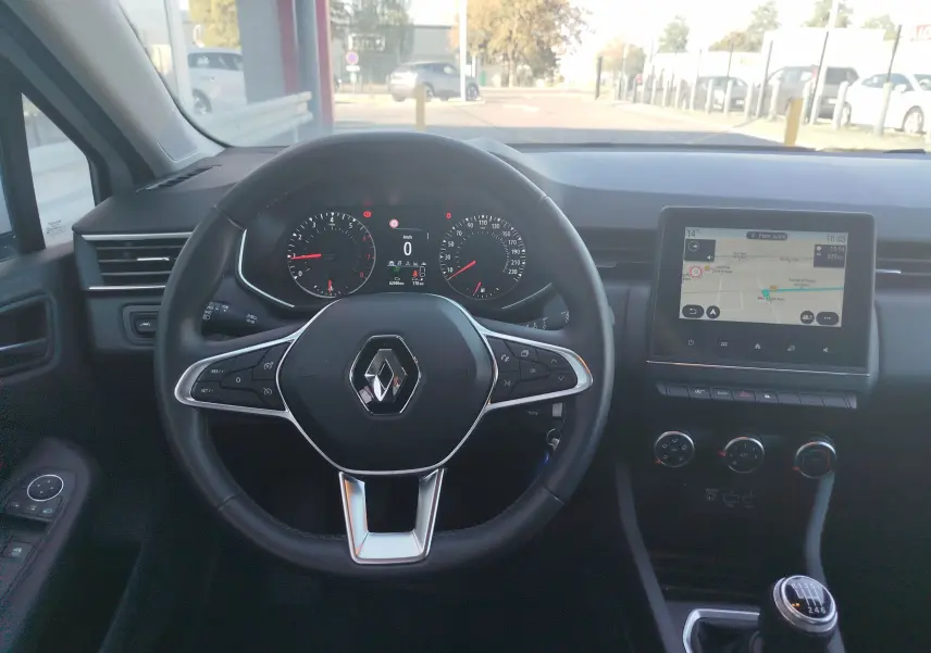 Vue intérieure centrée sur le volant et le tableau de bord d'une Renault Clio blanche de 2021 avec écran tactile et boîte manuelle.