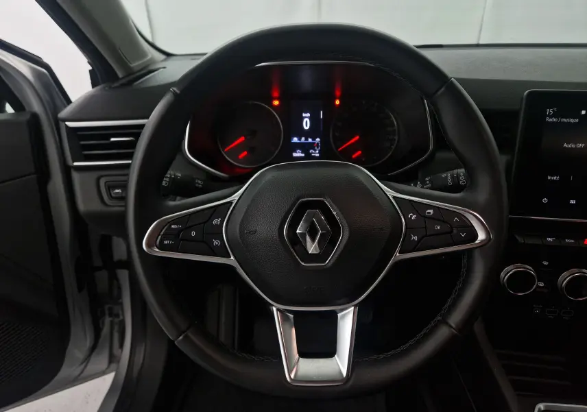 Volant en cuir noir avec logo Renault au centre, tableau de bord numérique et écran tactile sur Renault Clio V gris platine, vue intérieure frontale.