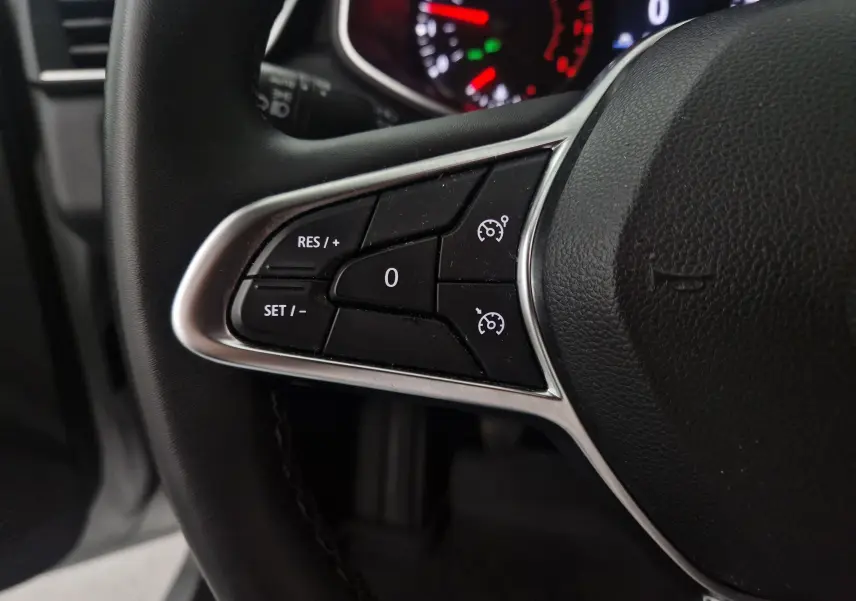 Gros plan sur les commandes de régulateur de vitesse à gauche du volant d'une Renault Clio V gris platine, tableau de bord en arrière-plan.