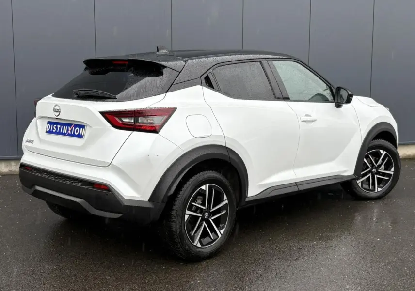 Nissan Juke blanc nacré en 3/4 arrière droit, toit noir contrasté et jantes alliage 17 pouces sous la pluie.