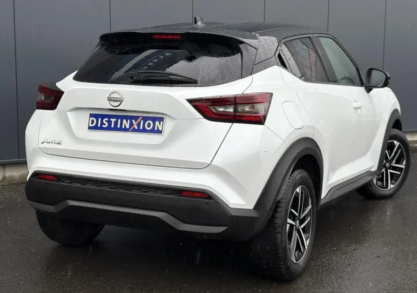 Vue 3/4 arrière droite du Nissan Juke blanc nacré 2025 avec jantes alliage et toit noir contrasté.
