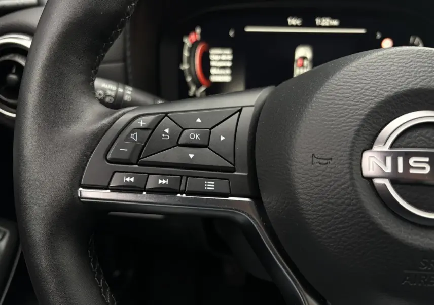Gros plan sur le volant en cuir noir du Nissan Juke 2025 avec commandes multifonctions et tableau de bord digital flou.