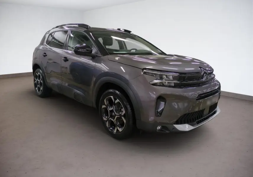 Vue 3/4 avant d'un Citroën C5 Aircross Hybrid gris Platinium avec jantes alliage bi-ton et barres de toit noires.