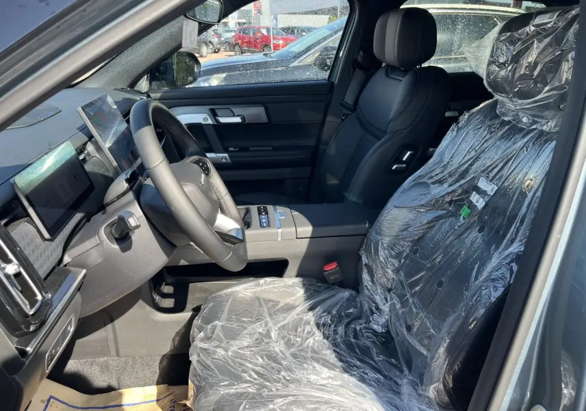 Vue intérieure côté conducteur du JAECOO J7 1.5 SHS-P gris olive, sièges noirs protégés par film plastique.