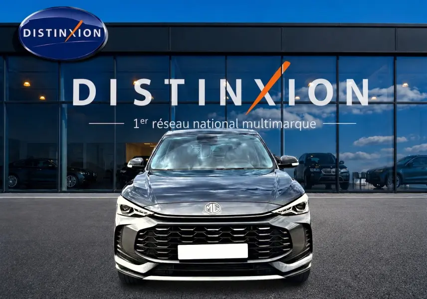 Vue avant du MG ZS 1.5 hybrid 197 Camden grey, avec calandre noire et phares LED, devant une vitrine Distinxion.