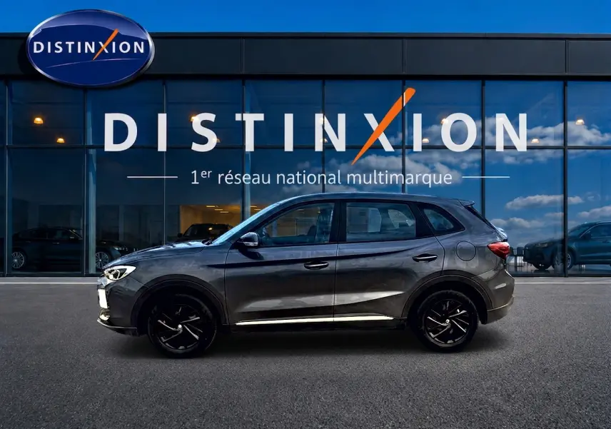 Vue de profil côté gauche du SUV MG ZS Camden grey 2026 garé devant une vitrine Distinxion.