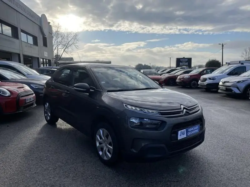 Vue 3/4 avant d'une Citroën C4 Cactus gris foncé métal 2019, avec ses phares étirés et calandre distinctive.
