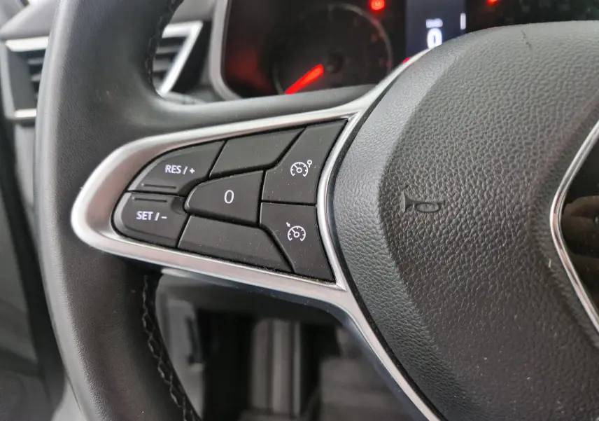 Gros plan sur les commandes de régulateur de vitesse à gauche du volant noir d'une Renault Clio V gris platine.