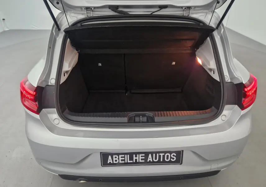 Coffre ouvert vu de l'arrière d'une Renault Clio V gris platine avec feux arrière allumés et intérieur de coffre noir.