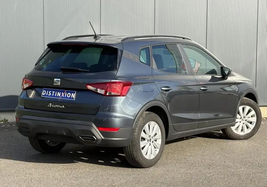 Vue 3/4 arrière droite d'un SEAT Arona gris magnétique 2024 avec barres de toit noires et jantes alliage 16 pouces.