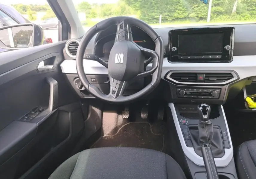 Intérieur du SEAT Arona 2024 vu de face, volant cuir multifonction, écran tactile et levier de vitesse manuel visibles.