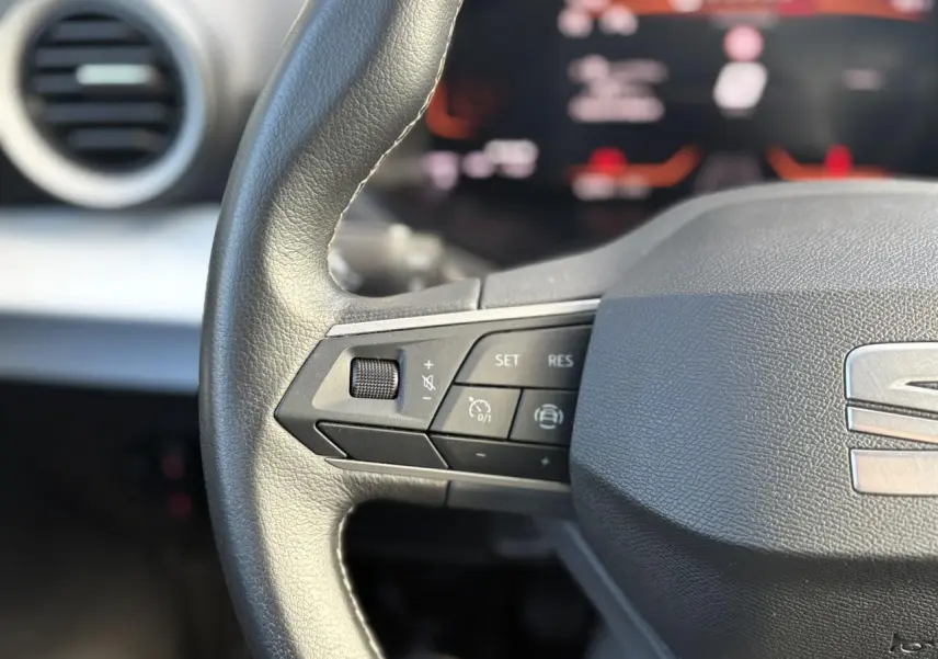 Gros plan sur le volant cuir multifonction gris du SEAT Arona 2024 avec commandes de régulateur et logo central visible.