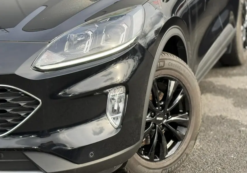 Gros plan sur l’avant droit du Ford Kuga noir Obsidien 2024, mettant en valeur le projecteur LED et la jante alliage noire.
