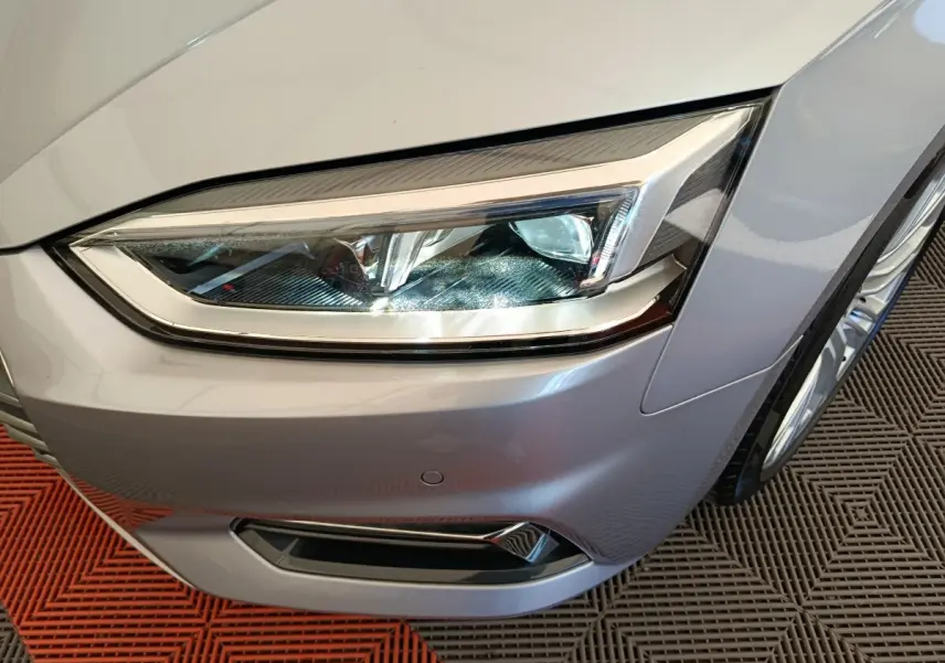 Gros plan sur le phare avant droit d'une Audi A5 gris clair, mettant en valeur les lignes nettes et les détails LED.