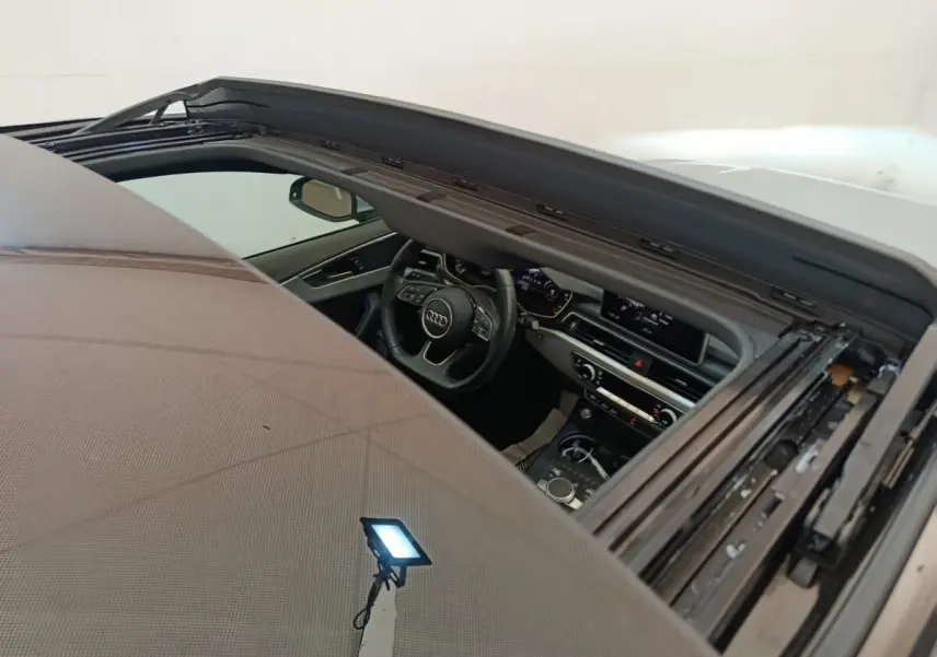 Vue intérieure par le toit ouvrant ouvert d'une Audi A5 gris clair, montrant le tableau de bord et le volant multifonctions.