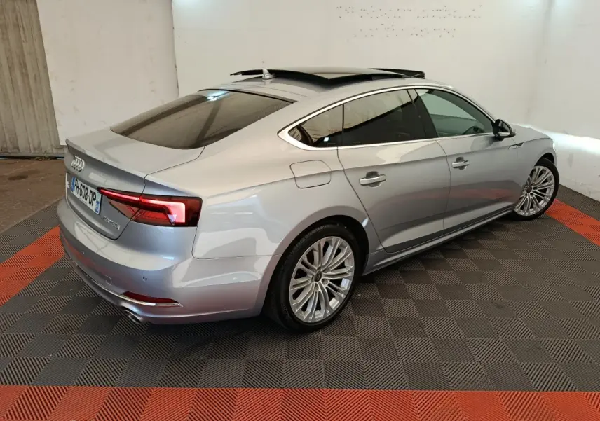 Audi A5 gris clair vue 3/4 arrière droit, toit ouvrant et feux arrière LED dans un garage intérieur.