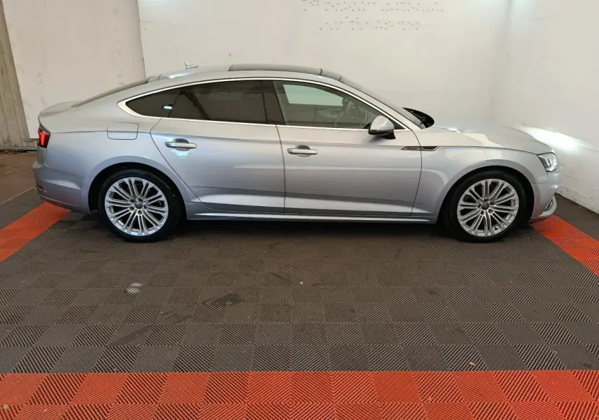 Profil côté gauche d'une Audi A5 gris clair 2019 avec jantes alliage et toit panoramique visible en intérieur.