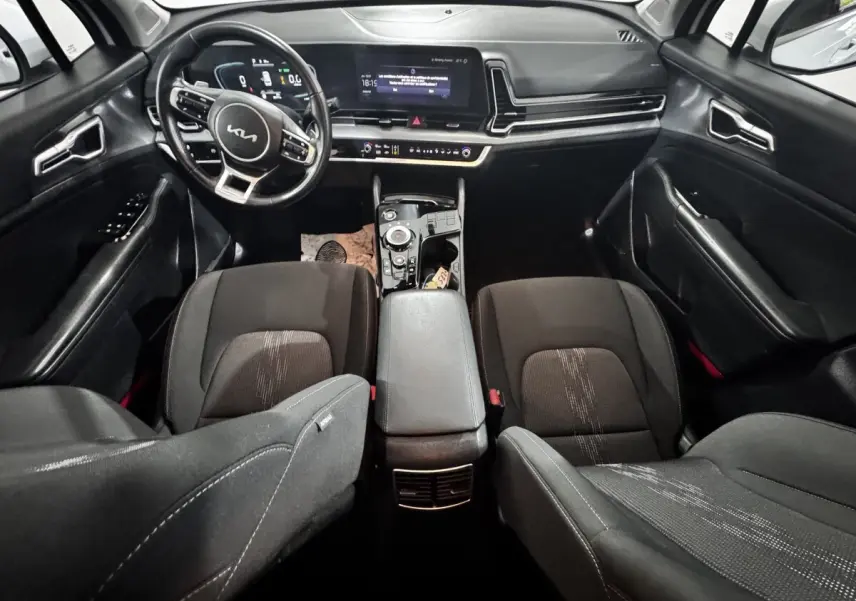 Vue intérieure avant du Kia Sportage blanc 2024, tableau de bord moderne avec écran tactile et volant multifonctions cuir.