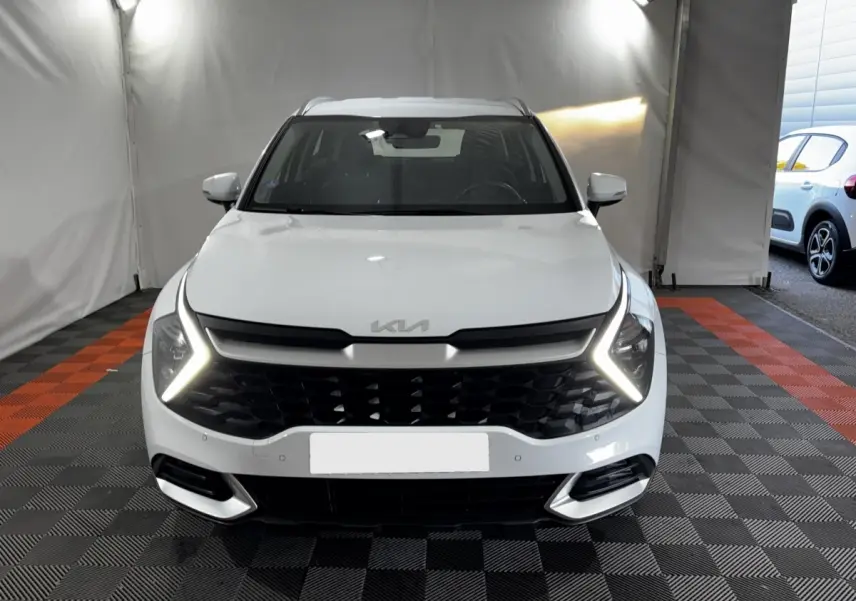 Vue frontale d'un Kia Sportage blanc 2024 avec feux diurnes LED en forme de flèche et calandre noire texturée.