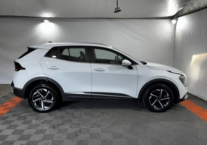 Profil droit d'un KIA Sportage blanc 2024 hybride essence, avec jantes noires et détails noirs contrastants.