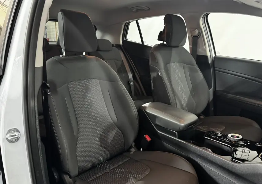 Vue intérieure côté gauche du Kia Sportage 2024 blanc, mettant en valeur les sièges avant noirs et la console centrale.